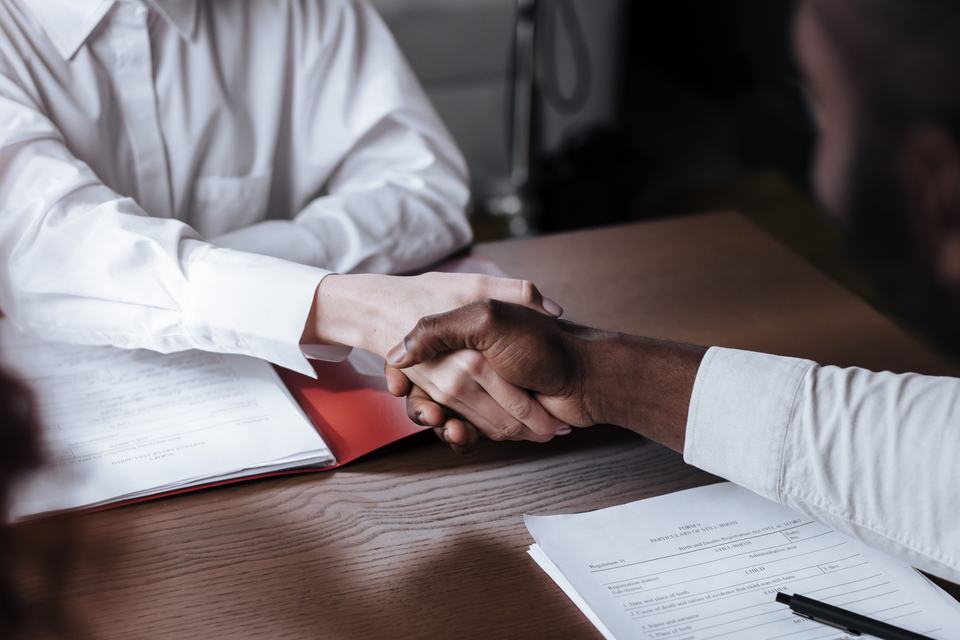 Two people shaking hands over paperwork, standing in for a buyer pricing a business on its owned traffic, not its ad spend.