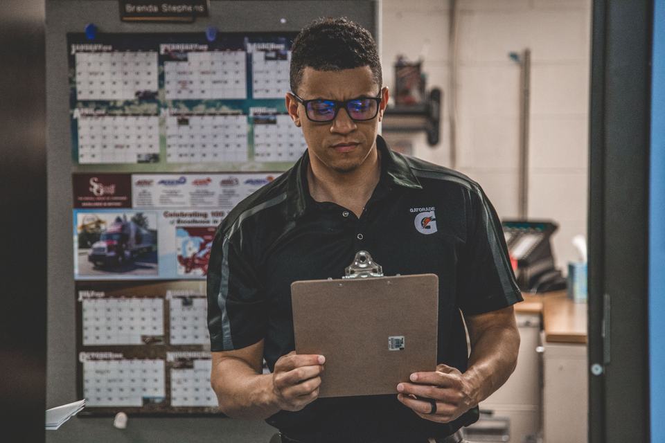 A worker in a shop reviewing a document on a clipboard, standing in for a contractor checking their licensing paperwork against their Google listing.