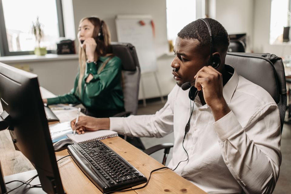 A focused office worker on a headset at a busy desk, standing in for staff racing to call back a shared lead before a competitor does.