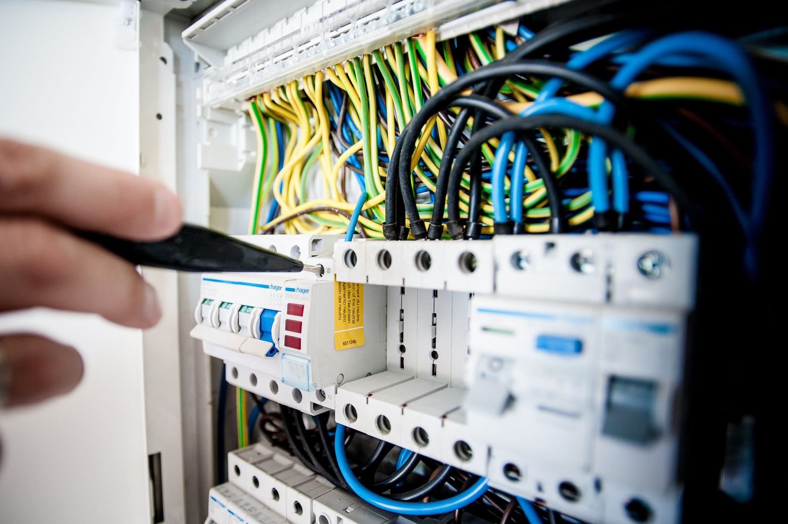 An electrician's hand working inside an open circuit panel, standing in for the real job a crew needs to document without slowing down.
