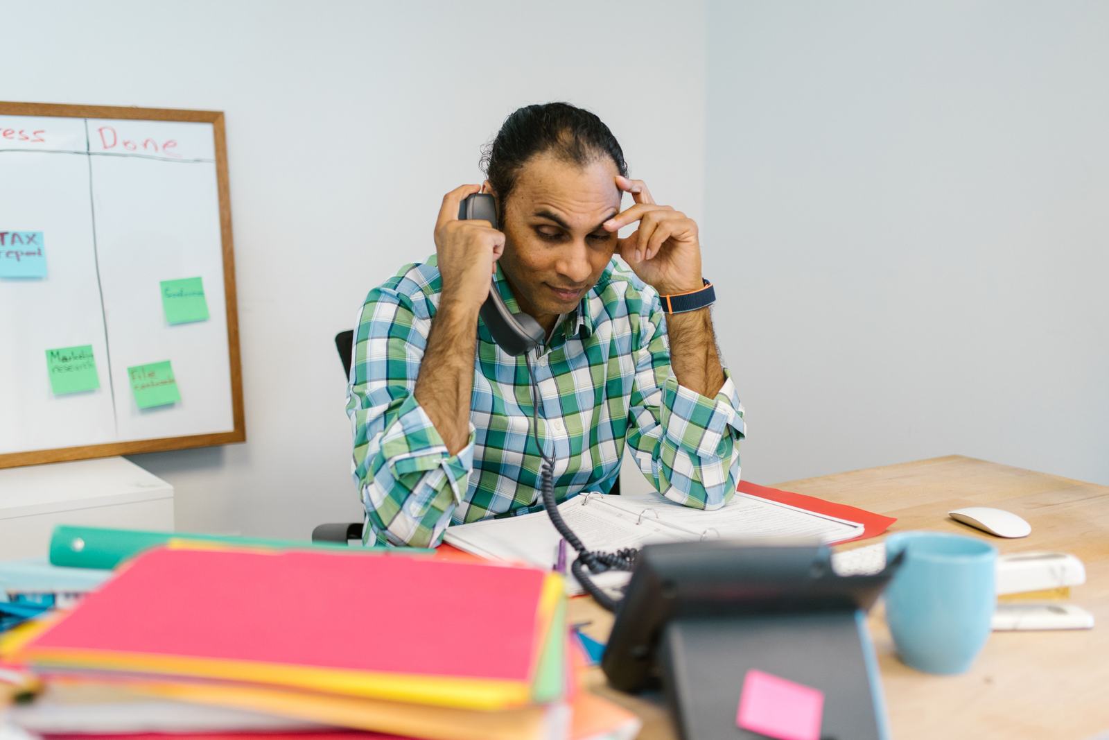 A stressed office worker on the phone surrounded by paperwork, standing in for staff chasing unqualified shared leads.