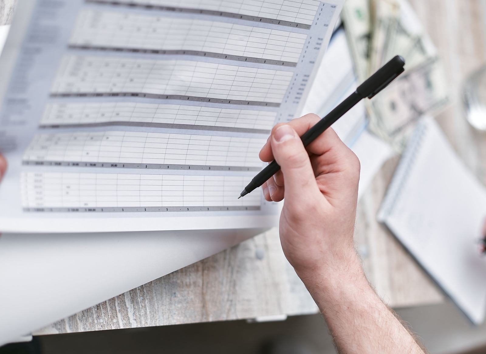 A close-up of a hand reviewing a budget spreadsheet with a pen, standing in for a business owner tapering shared lead spend line by line.