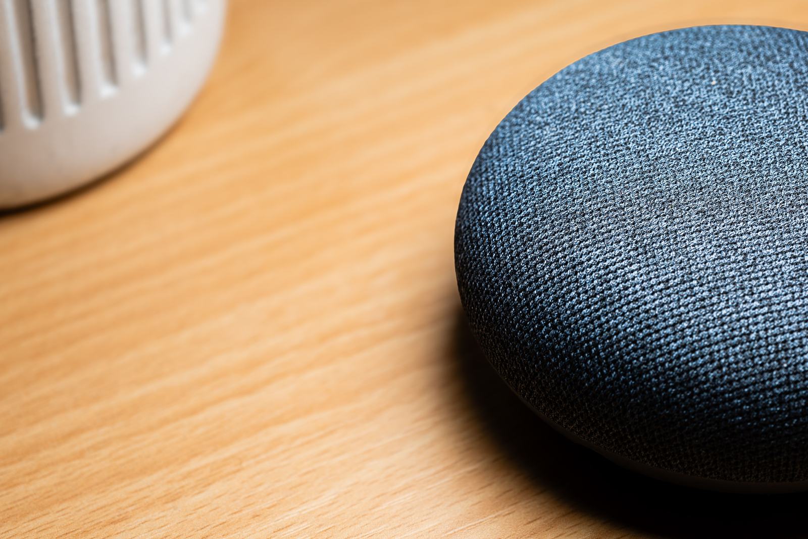 A close-up of a smart speaker on a wooden table, standing in for a voice search asking for a local business.