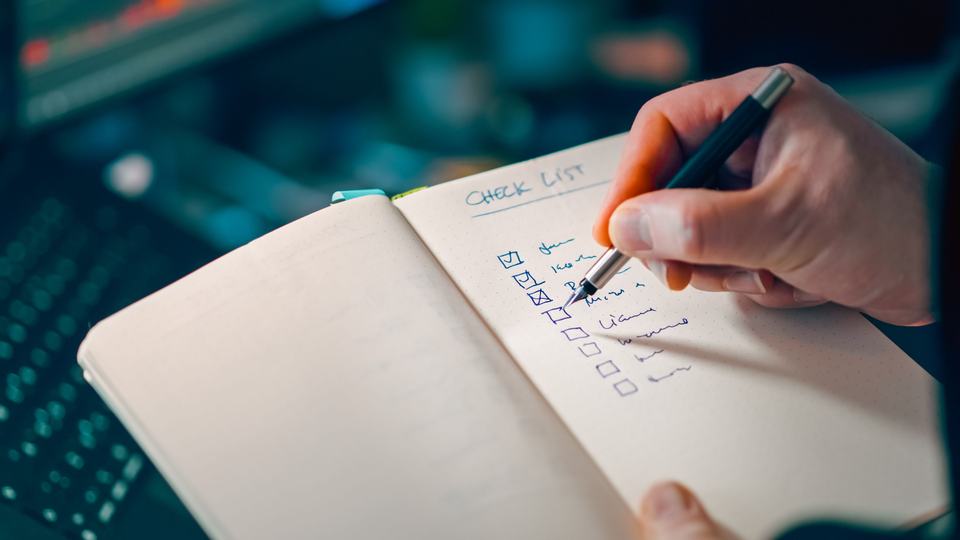 A hand writing a tick-box checklist in an open notebook, standing in for a log of each AI answer